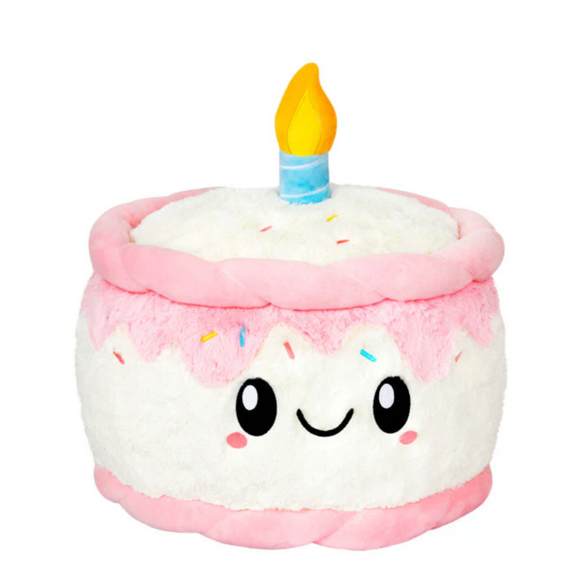 Happy Birthday Cake Snackers plush toy with smiling face, pink icing, sprinkles, and a yellow candle on top.