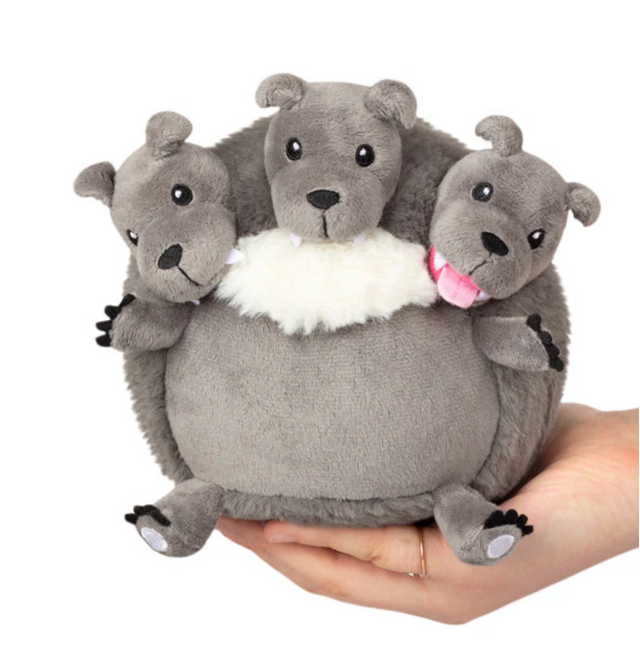 Hand holding Cerberus Snackers plush toy with three gray dog heads showing different expressions in soft fabric.