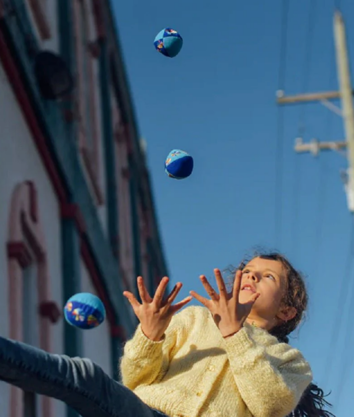 Girl juggling vividly colored balls outdoors with a clear sky backdrop using the Juggling Balls set.