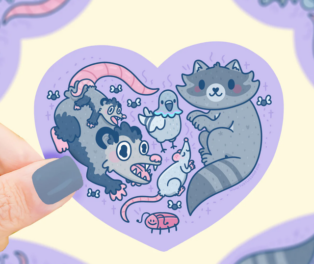 Hand holding Stinky Trash Animals Heart Sticker featuring cute trash animals inside a purple heart shape.