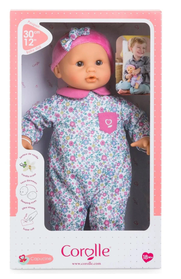 Calin Capucine baby doll in floral outfit with pink hat, soft vinyl limbs, and gentle vanilla scent in boxed packaging.