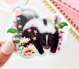 Skunk Sticker showing a cute sleepy skunk surrounded by pink and white flowers on glossy vinyl.