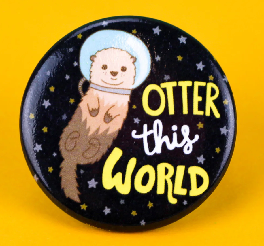 Otter This World Button pin with floating otter in space helmet and stars on black background.