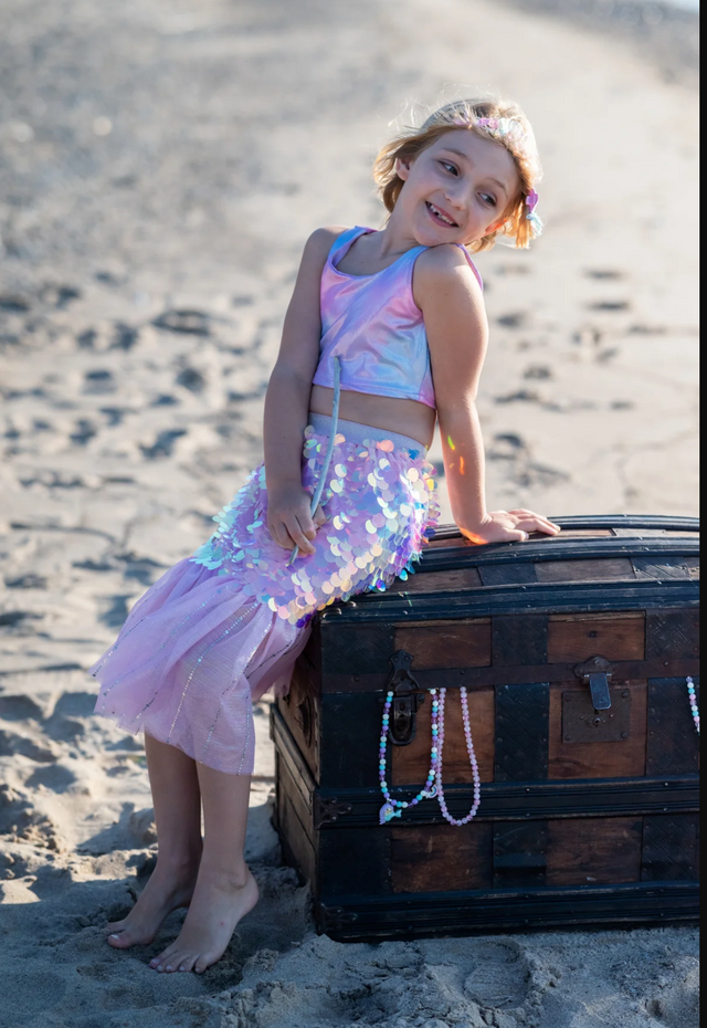 Bling Bling Mermaid Skirt & Hairclip | Pink worn by smiling girl sitting on treasure chest at beach.