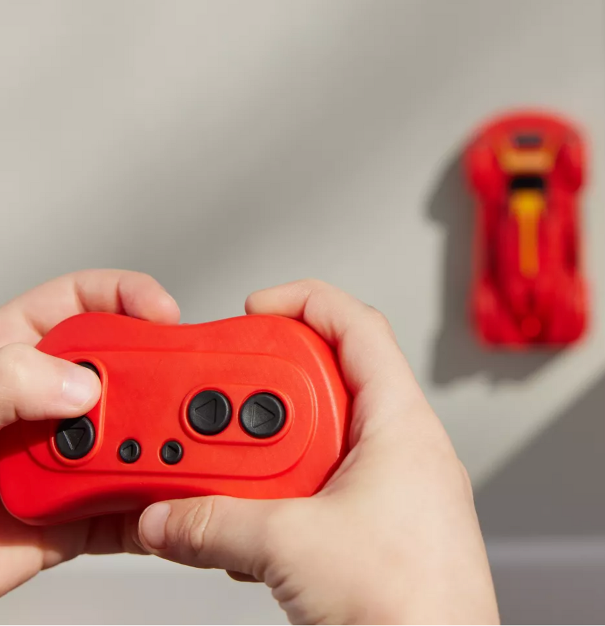 Hands holding a red remote controlling the Air Hogs Zero Gravity Sprint Wall Climber car on a wall surface.