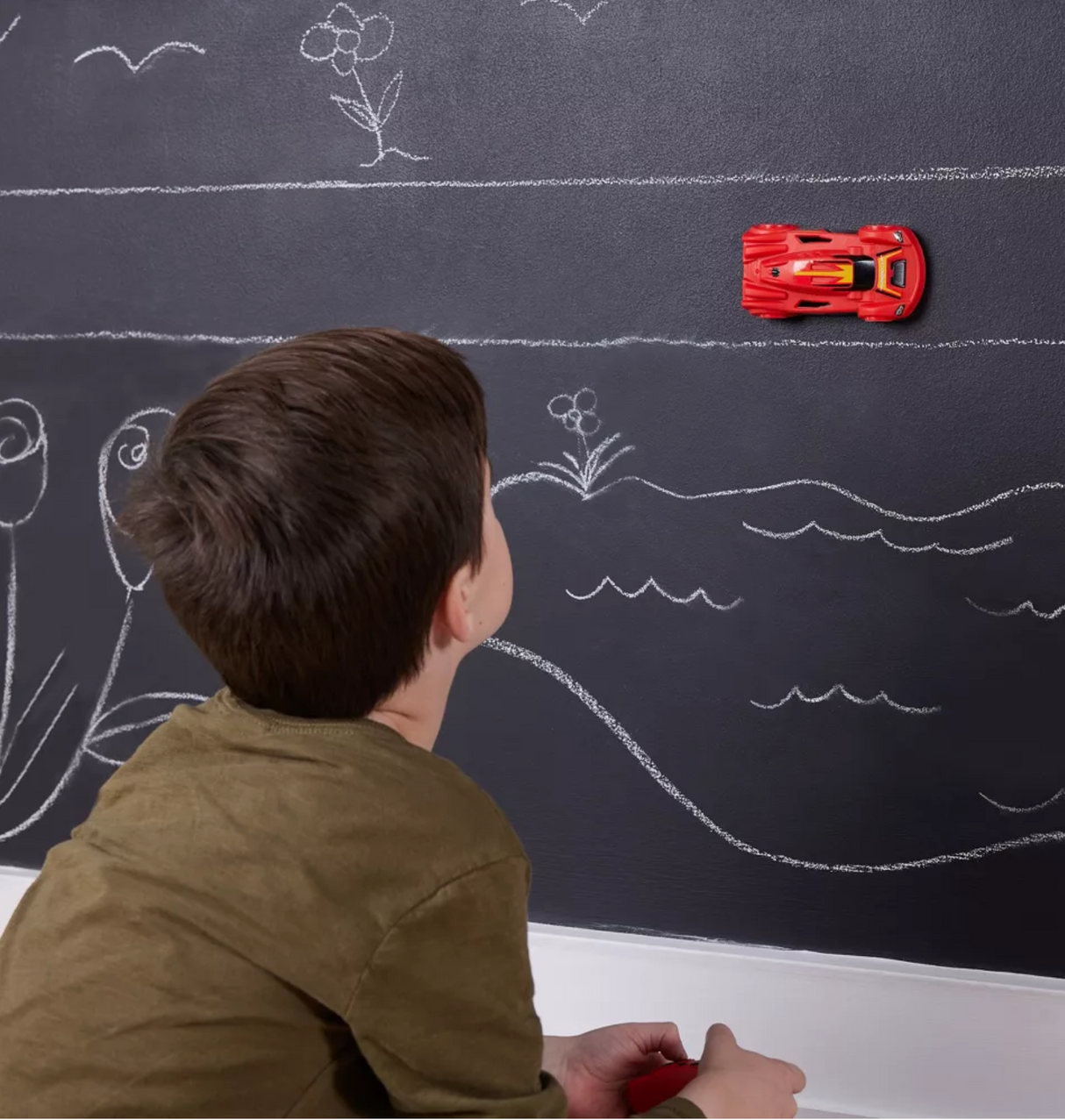 Young boy watches red Air Hogs Zero Gravity Sprint Wall Climber race on chalkboard wall with drawn scenery.