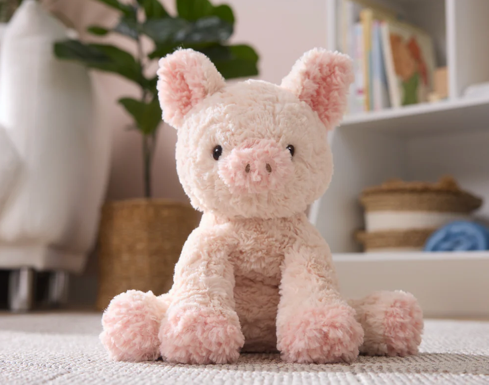 Cozys Pig plush with soft peachy-pink fur, button nose, floppy limbs, and a springy curly tail for hugging and play.