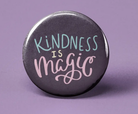 Button | Kindness is Magic with pastel text on a dark background, promoting positivity and kindness on a purple surface.