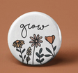 Button | Grow Flowers round pin featuring hand-drawn floral design and the word "grow" in cursive on white background.