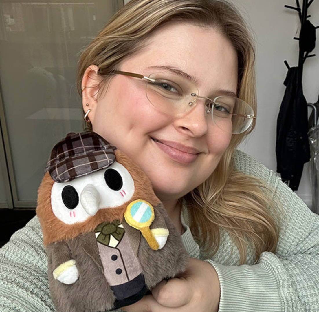 Smiling woman holding Alter Ego | Plague Doctor Detective plush toy dressed in Victorian detective outfit with magnifying glass.