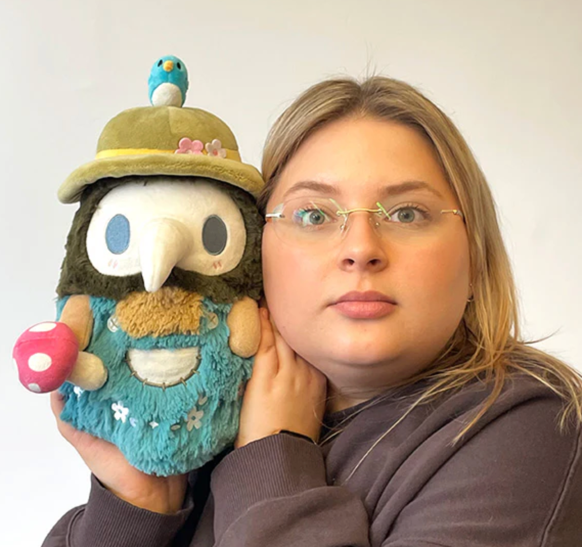Person holding the Spring Mushroom Plague Doctor plush with pastel colors, mushrooms, and a small bird on the hat.