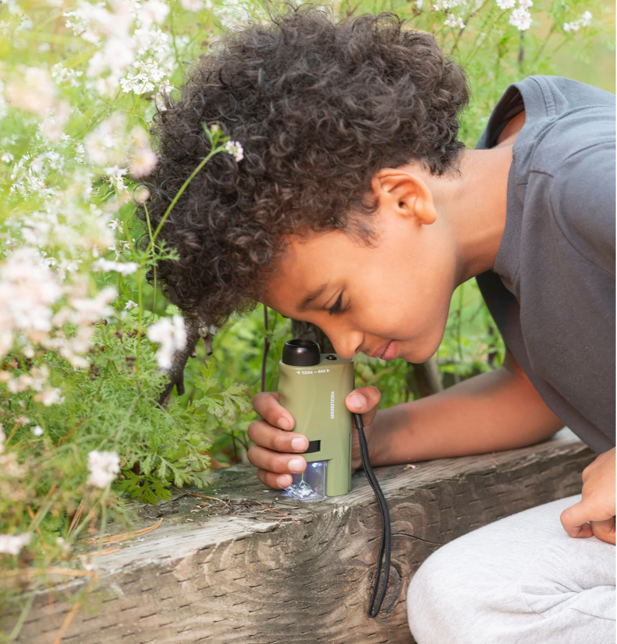 Young child exploring plants outdoors using the Huckleberry Pocket Microscope with LED lighting and adjustable zoom.