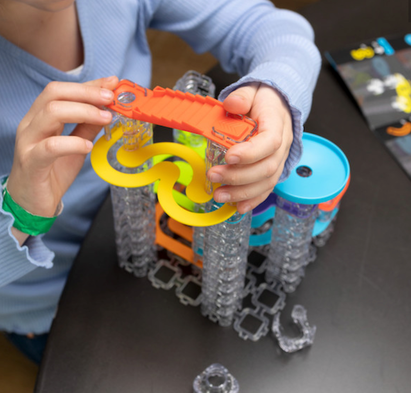 Child assembling colorful pieces of the Trestle Tracks Builder Set marble run on a black surface.
