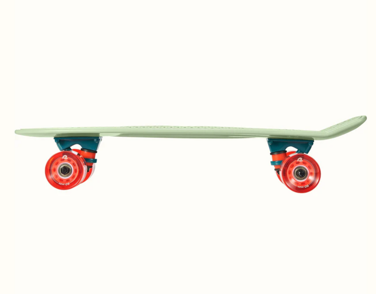 Quip Mini Cruiser Skateboard Green Tea side view showing flexible plastic deck with bright orange wheels for smooth rides.