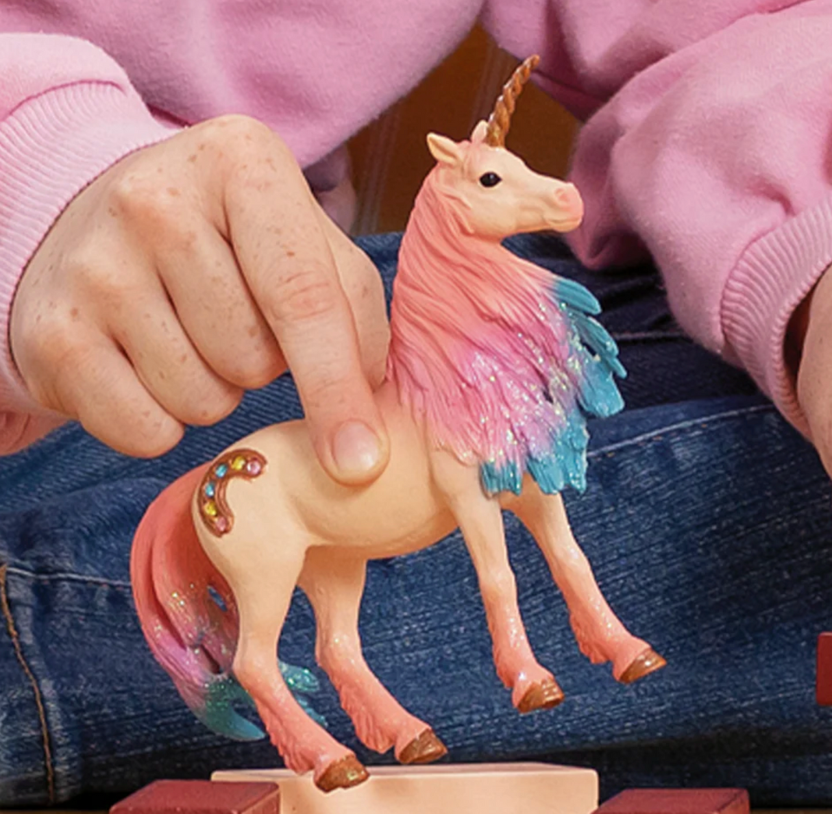 Bayala | Marshmallow Unicorn Mare figurine with pink and blue mane held by a child wearing a pink sweater.
