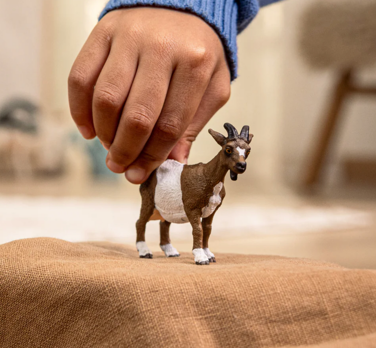Child’s hand holding the Goat toy with a white and brown coat and star-shaped spot on its forehead.
