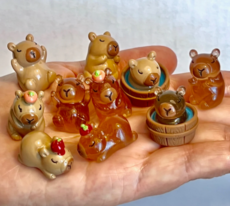 Capybara Miniature Figurine showing assorted cute small capybara designs resting and playing on a hand.