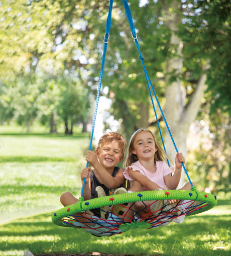 Two children enjoying playtime on a colorful Dreamcatcher Swing hanging from tree branches outdoors.