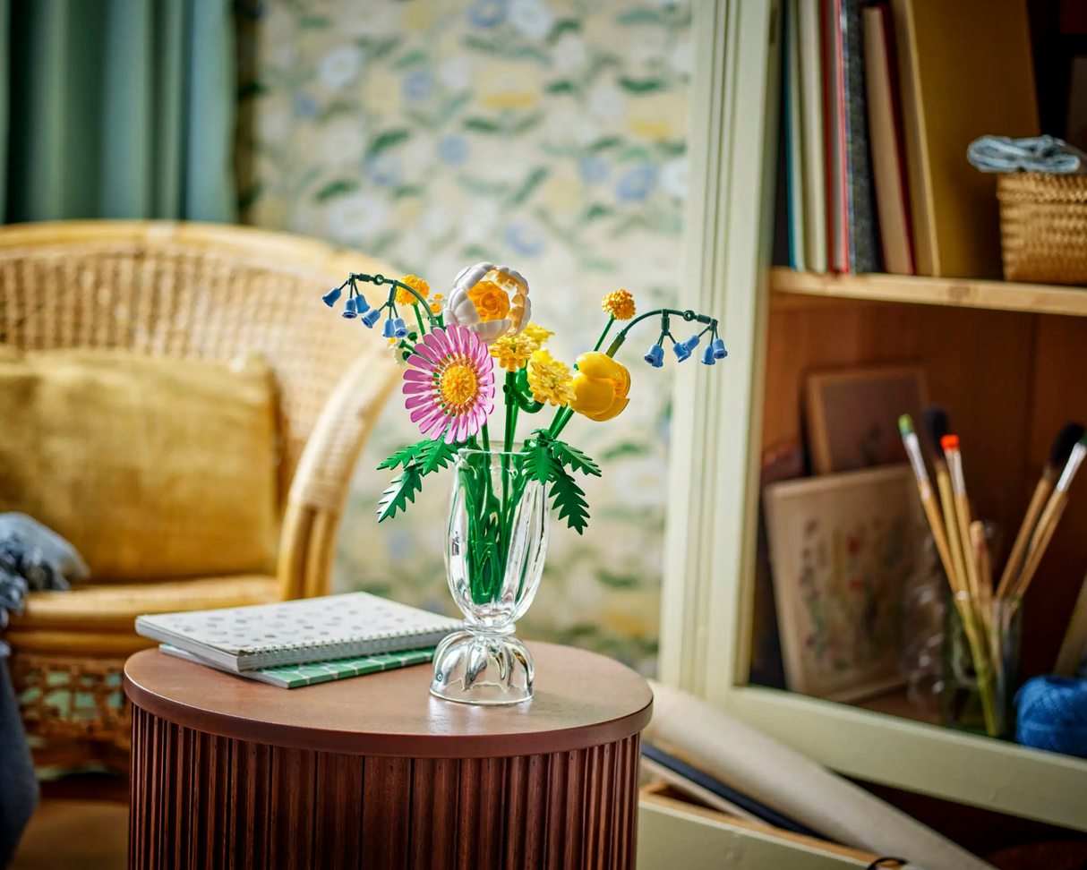 Botanicals Petite Sunny Bouquet in clear vase displayed on wooden table with cozy room background and bookshelves.