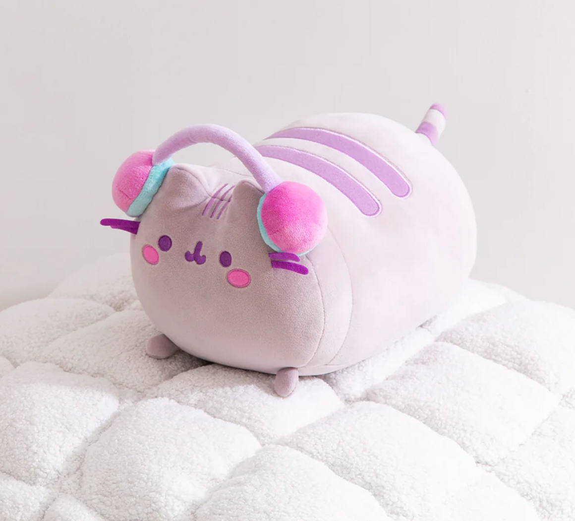 Pusheen Gamer Log Squisheen plush with purple stripes, pink cheeks, and colorful headphones lounging on a soft blanket.
