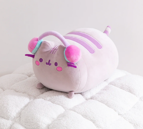 Pusheen Gamer Log Squisheen plush with purple stripes, pink cheeks, and colorful headphones lounging on a soft blanket.