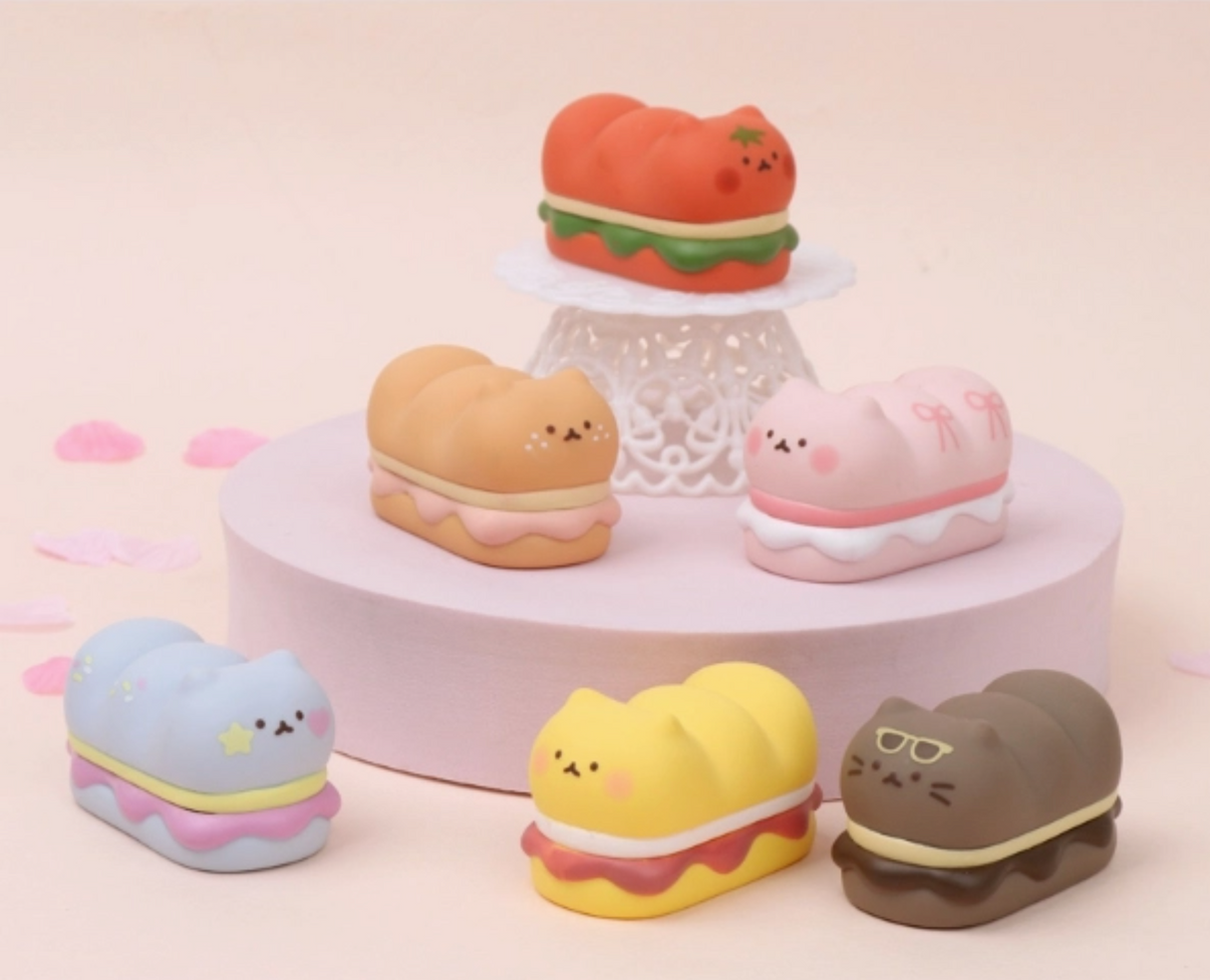 Six colorful cat-shaped figures inspired by desserts and sandwiches displayed on pastel platforms