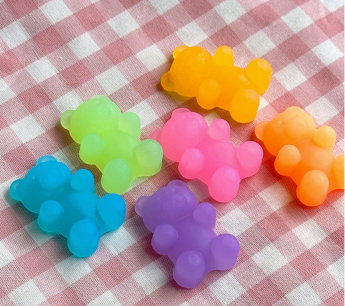 Six colorful gummy bear shaped erasers arranged on a pink and white checkered fabric background