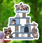 Cute sticker showing a raccoon and opossum playing and resting on a multi-level cat tree structure