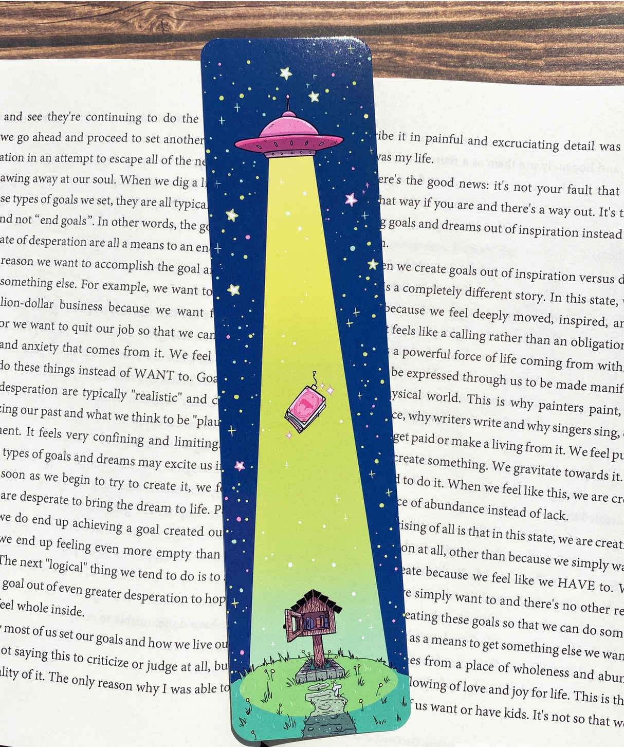 Colorful UFO and house design on glossy double-sided bookmark lying on open book pages