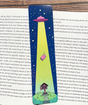 Colorful UFO and house design on glossy double-sided bookmark lying on open book pages