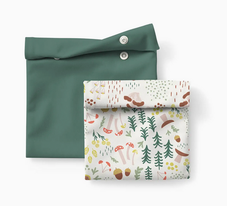 Two reusable Snack and Sammy pouches, one solid green and one with a colorful mushroom forest pattern, laid flat.