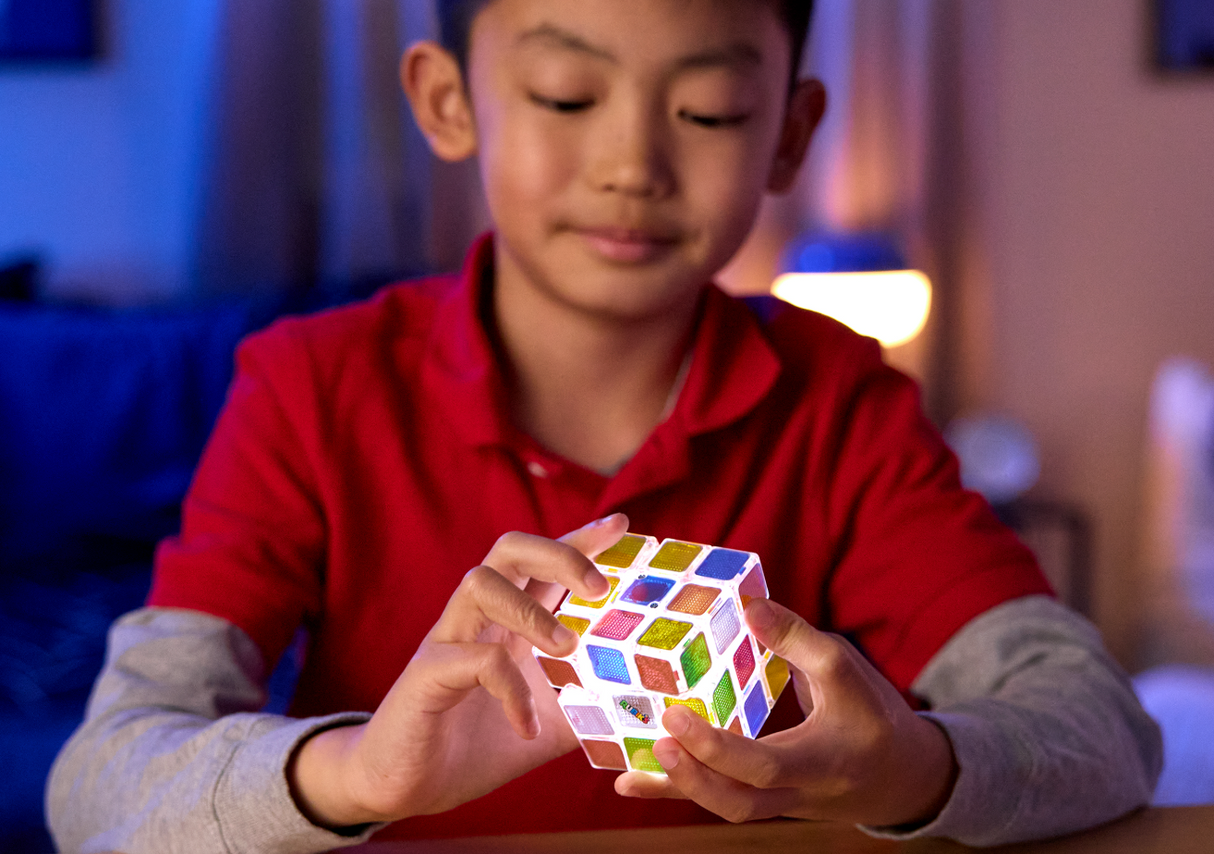 Young boy focused on solving a glowing Rubik's Cube Pulse with colorful illuminated sides in a cozy room setting
