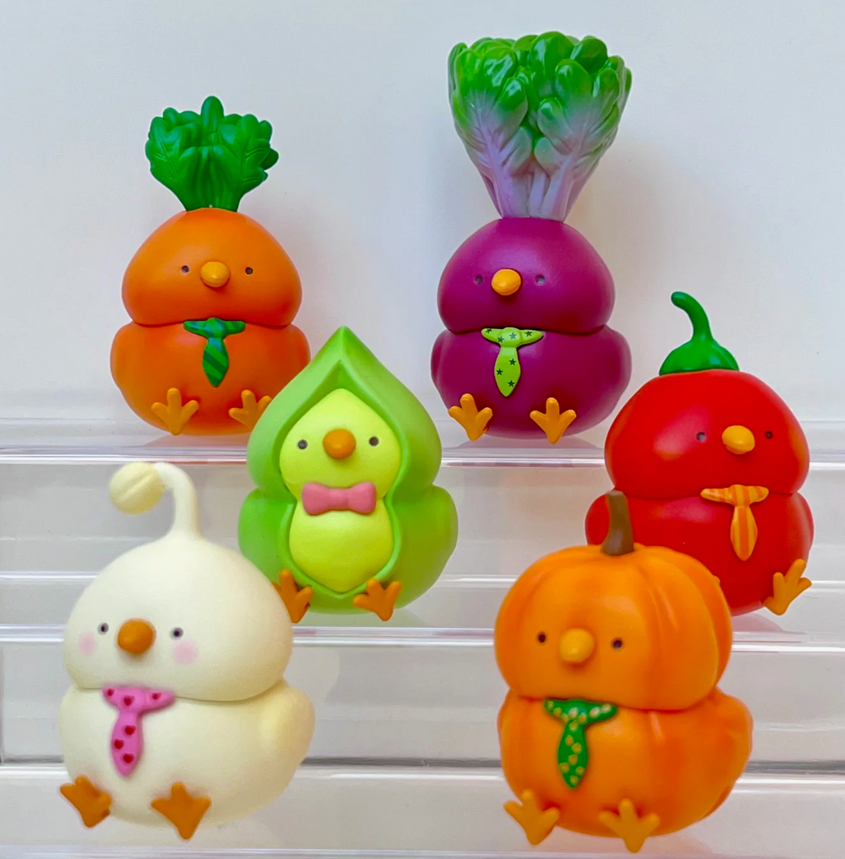 Five colorful vegetable-inspired bird figurines wearing ties, displayed on clear stands against a white background