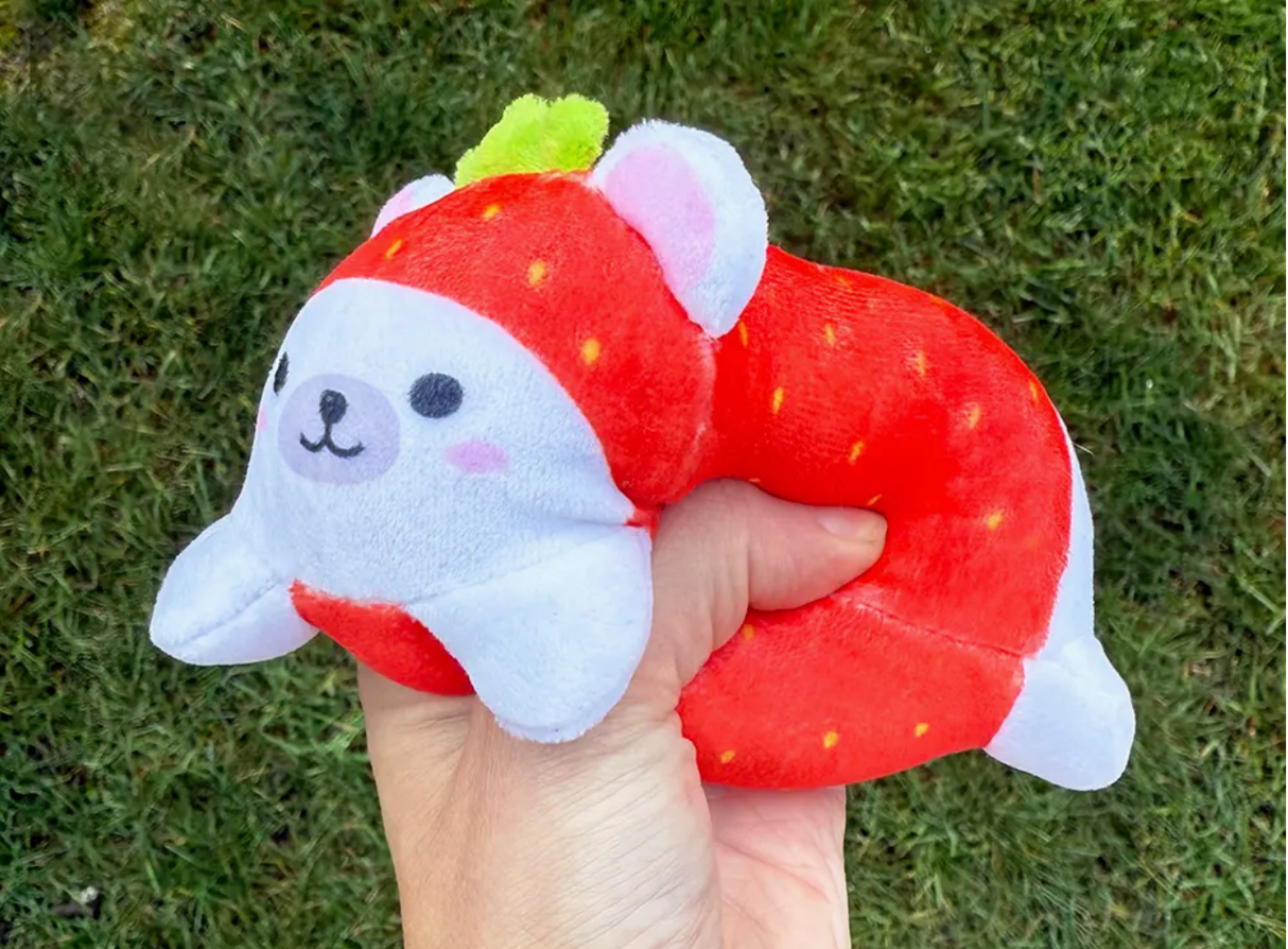 Hand squeezing a soft, strawberry-themed Sand-A-Roos Friend plush with a calming texture and subtle grainy sound.