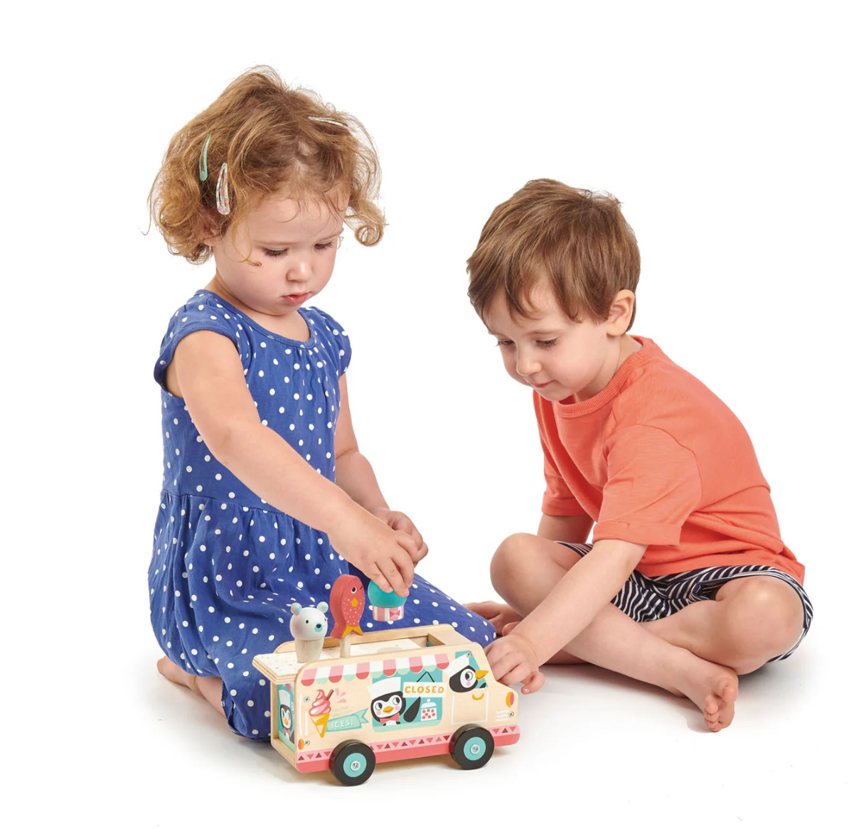 Two young children playing with a colorful wooden gelato van toy featuring penguins and ice cream on the roof