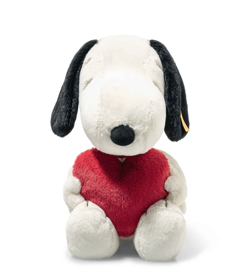 Plush Snoopy holding a bright red heart with embroidered eyes and soft textured fur sitting upright.