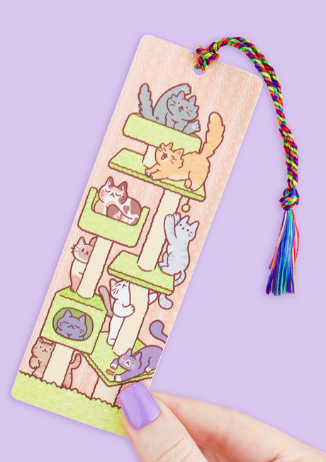 Bookmark featuring playful cats on a tower with a colorful rainbow tassel against a purple background