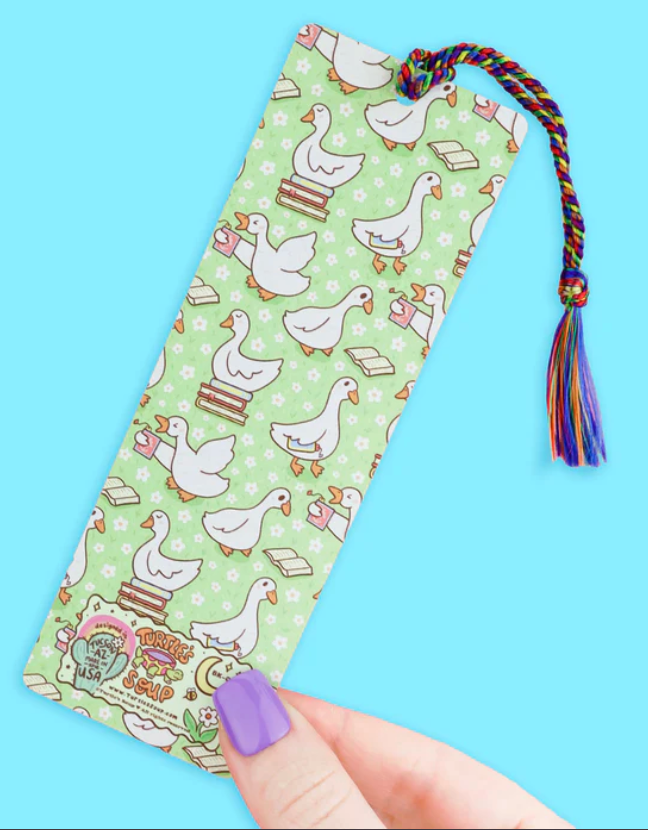 Colorful bookmark with playful ducks and books design, featuring a rainbow tassel and held against a blue background.