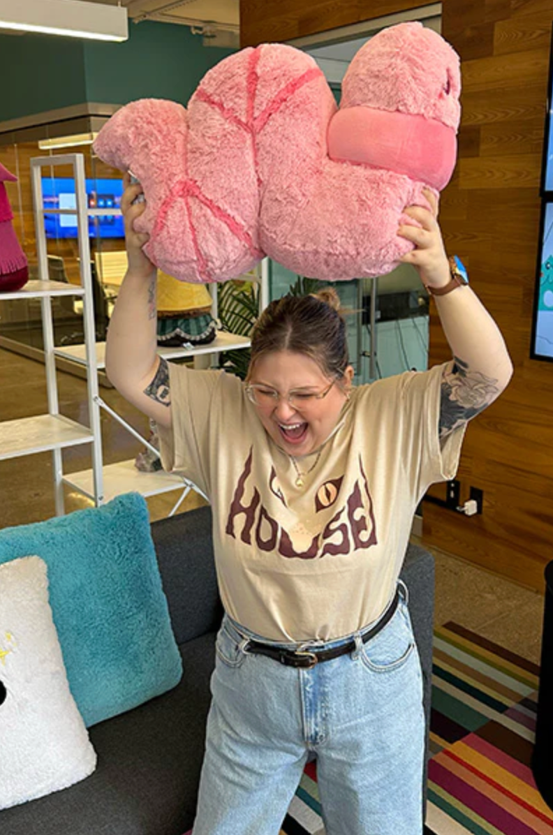 Person holding a large soft pink worm plush toy above their head inside a cozy room setting