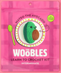Pink packaging of The Woobles Mateo the Avocado crochet kit with an image of the crocheted avocado on a decorative plate