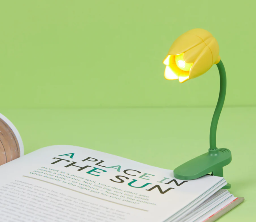 Miniature tulip-shaped book light with flexible arm clipped to a book, illuminating the page for nighttime reading