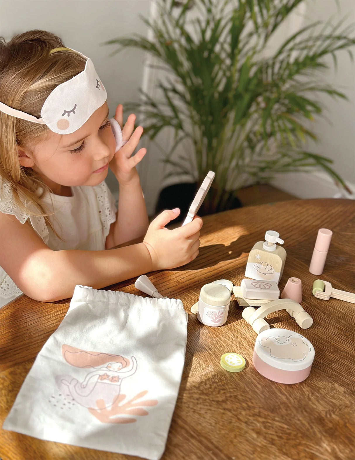 Child playing with Spa Retreat Set including eye mask, lotion, scrub, mirror, and massage accessories on wooden table.