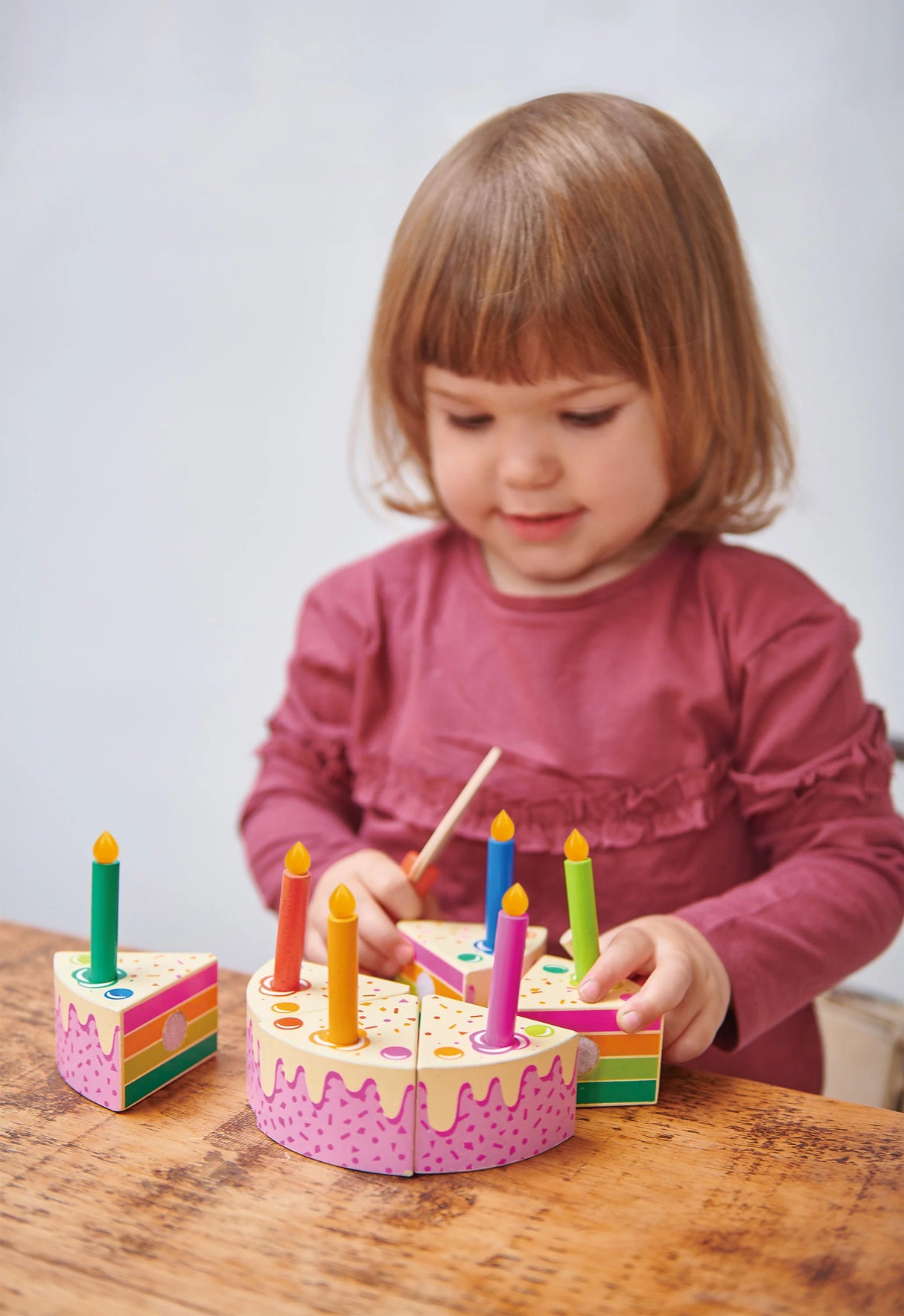 A child playing with a wooden Rainbow Birthday Cake toy with colorful candles on a wooden table.