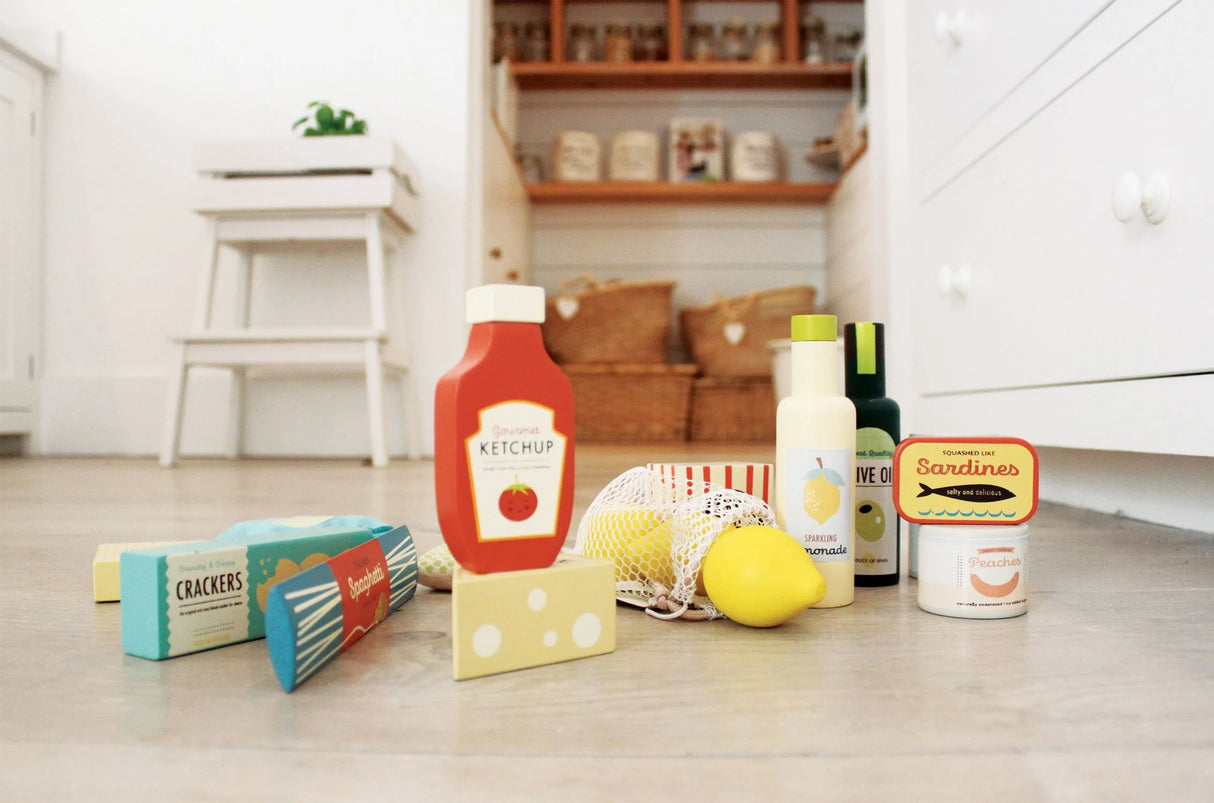 Supermarket Grocery Set with toy ketchup, cheese, crackers, lemons, olive oil, sweets, and cat food on kitchen floor.
