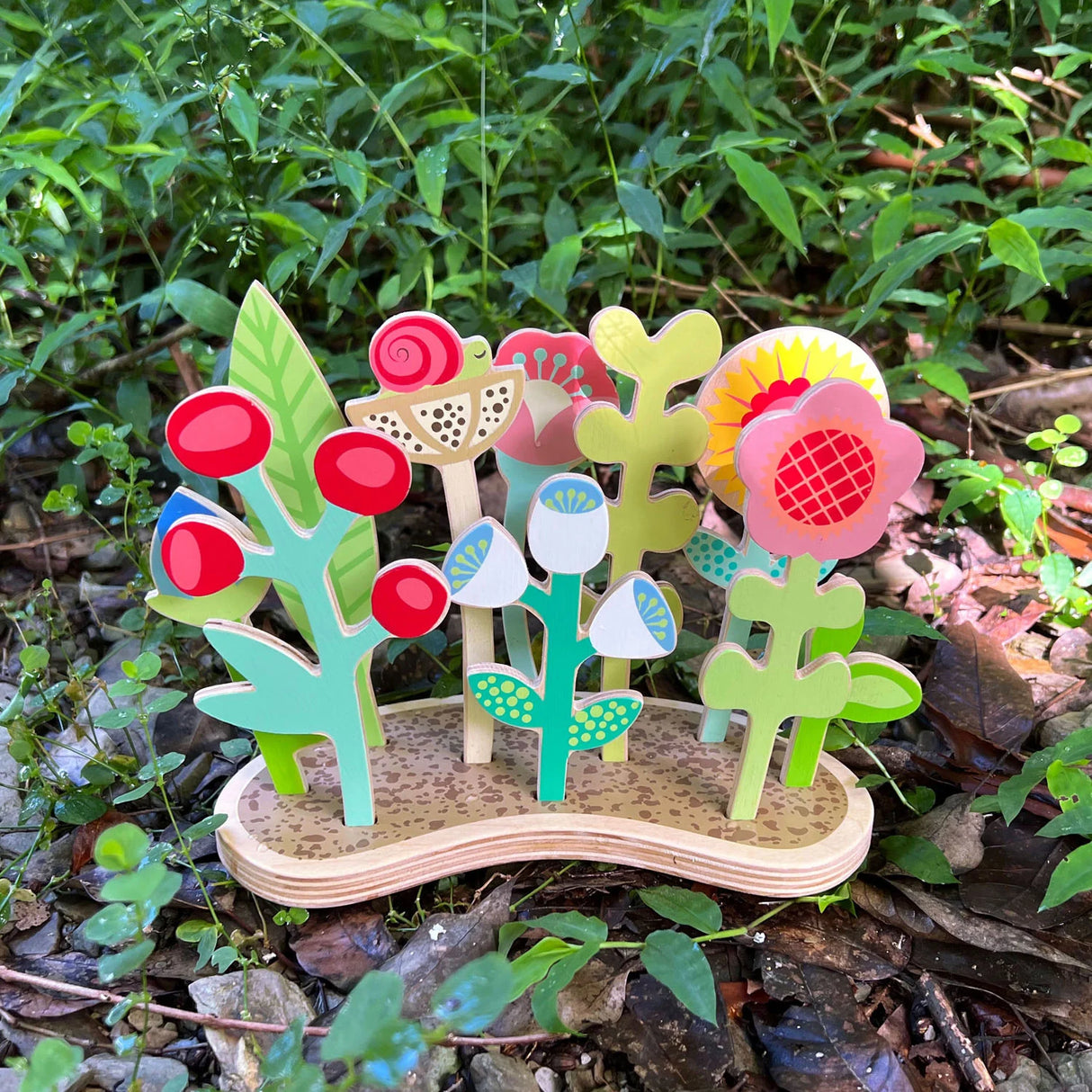 Flower Bed wooden toy with 10 colorful plywood plants showing various growth stages on a natural base outdoors.