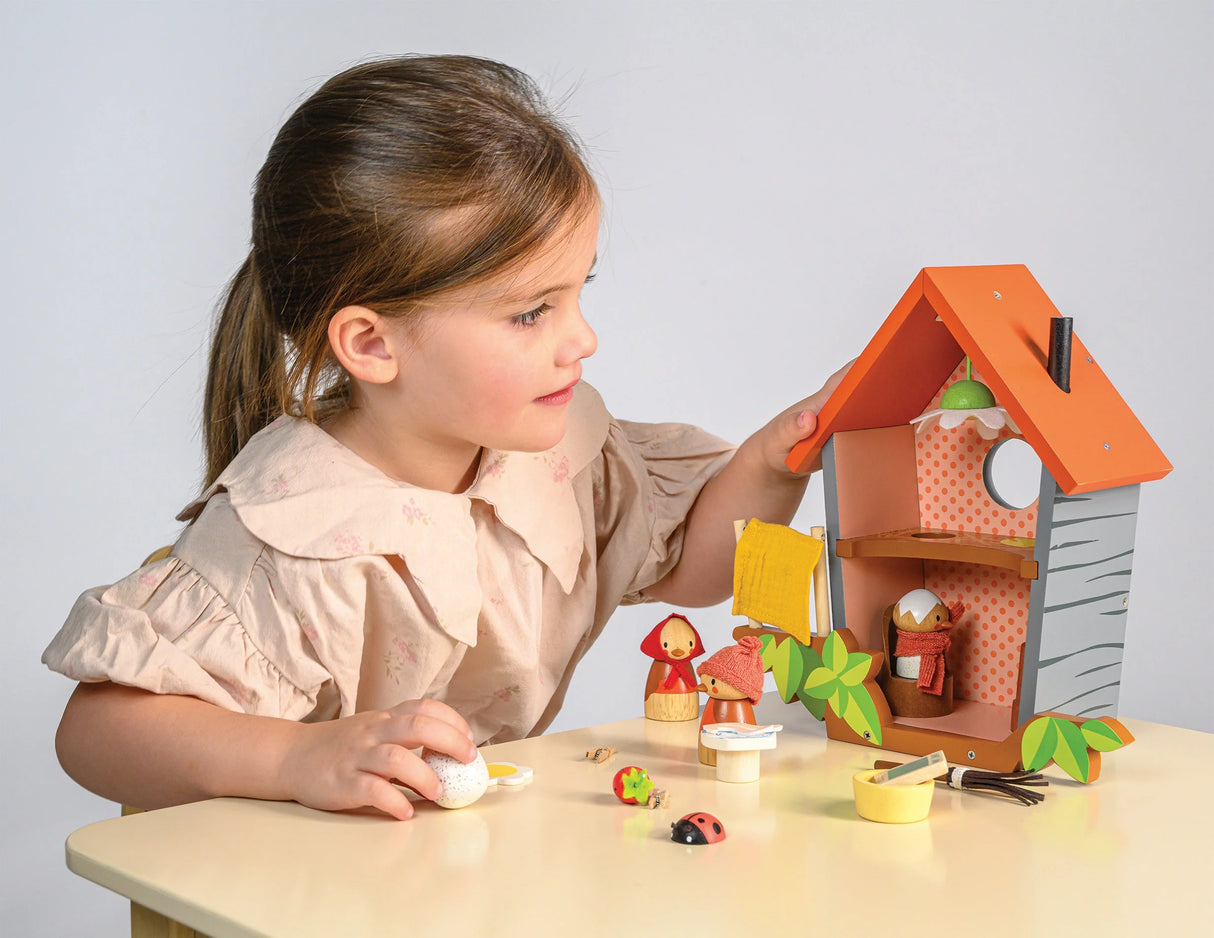 Young girl playing with colorful wooden Robin's Nest Box toy featuring bird family and accessories on a table.