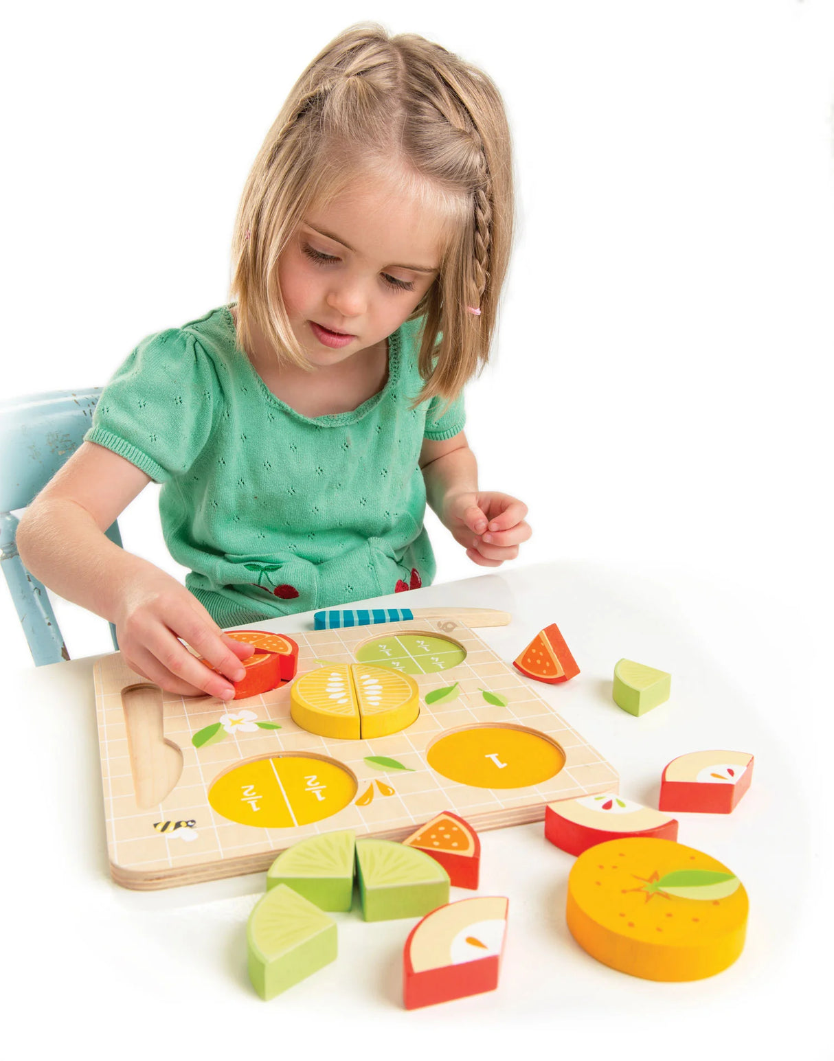 Child playing with colorful wooden Citrus Fractions set teaching fractions using fruit pieces and a cutting board.