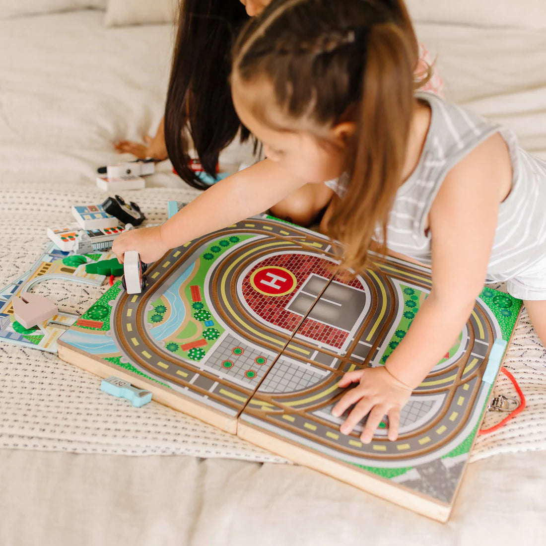 Two children playing with the colorful wooden Take Along Town playset featuring built-in tracks and vehicles.