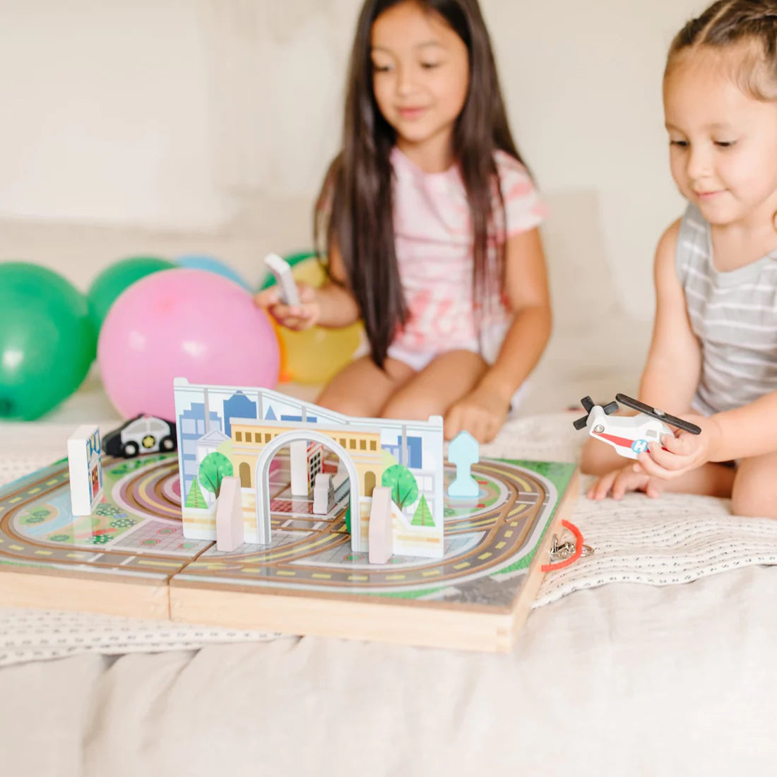 Two children playing with colorful wooden vehicles and city play pieces on the Take Along Town foldable play set.