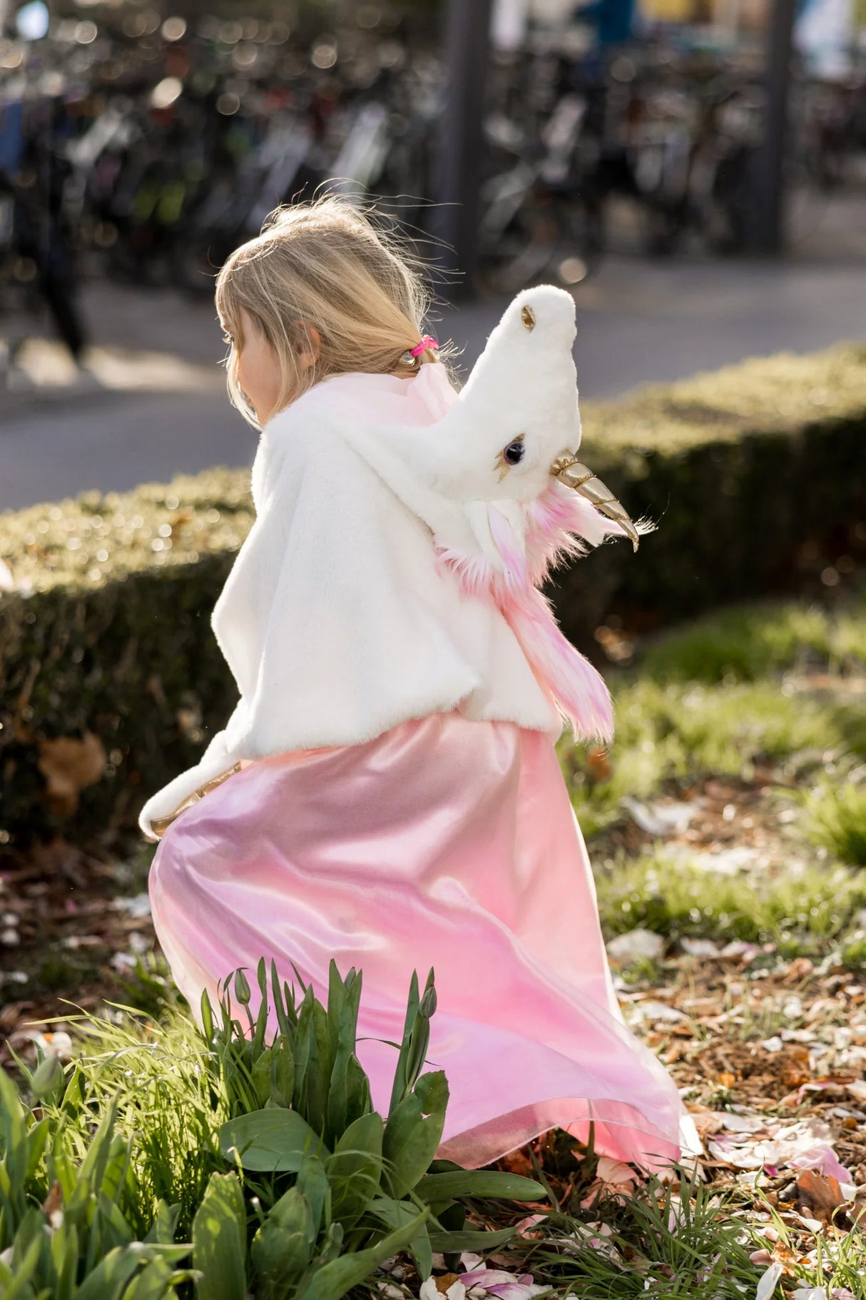 Child wearing Unicorn Cuddle Cape Size 4-6 with soft white fur, pink mane, and golden horn outdoors in sunlight.